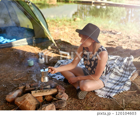 Morning coffee on the brew. Shot of a young woman making coffee over an open fire at a campsite. 120104603
