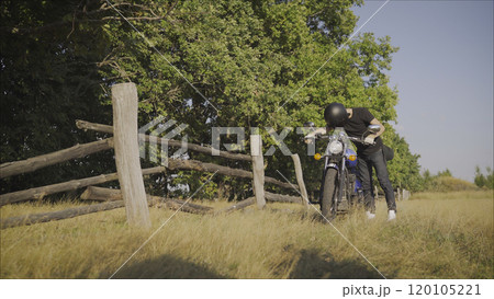 Motorcyclist pulls a broken bike. Motorcyclist rolls his motorcycle. Motorcyclist goes near his bike. Motorcyclist and bike on the road 120105221