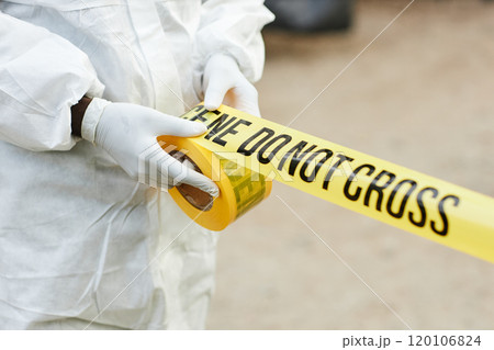 Close up of unrecognizable person wearing hazmat suit unrolling Do not cross tape outdoors and fencing off dangerous site, copy space 120106824