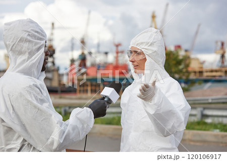 Portrait of young woman wearing protective suit giving interview to news reporter at industrial site outdoors Portrait of young woman wearing protective suit giving interview to news reporter at industrial site outdoors 120106917