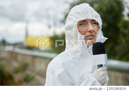 Portrait of young woman wearing hazmat suit and speaking to microphone while reporting on ecology news outdoors, copy space 120106924