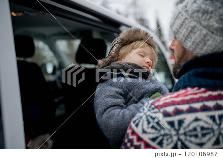 Father is putting his sleeping son into the car seat. The boy fell asleep from exhaustion after a walk in nature. Father is putting his sleeping son into the car seat. The boy fell asleep from exhaustion after a walk in nature. 120106987