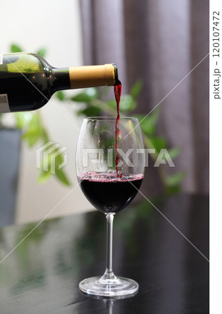 Wine is poured from a bottle into a glass. Red wine is poured into a glass. Wine is poured from a bottle into a glass. Red wine is poured into a glass. 120107472