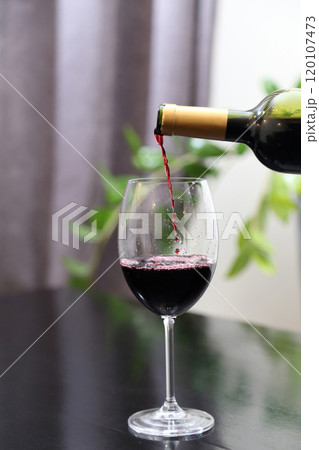 Wine is poured from a bottle into a glass. Red wine is poured into a glass. Wine is poured from a bottle into a glass. Red wine is poured into a glass. 120107473