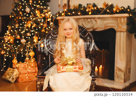 Happy little girl child with festive gift box sitting near Christmas tree and fireplace at home 120110314