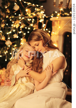 Happy young mother hugs child daughter near Christmas tree at home 120110334