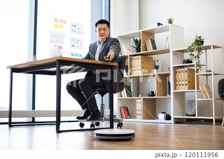 Asian businessman multitasking in modern office with robot vacuum cleaner 120111956