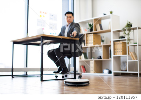 Asian businessman multitasking in office with robot vacuum cleaner 120111957