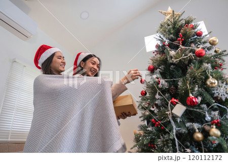Young Woman Joyfully Decorating Her Room for a Cozy Christmas Celebration with Festive Ornaments and Holiday Spirit Young Woman Joyfully Decorating Her Room for a Cozy Christmas Celebration with Festive Ornaments and Holiday Spirit 120112172
