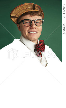 Portrait of young man with glasses, straw hat, and red bow tie, smiling brightly against green background with blank white space. 120112837