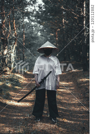 A mysterious warrior in a black mask and Asian hat holds a glittering katana sword in the forest. The scene exudes danger and adventure with a hint of Japanese culture. Warrior with katana. 120112882