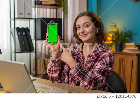Woman freelancer looking at camera and showing smartphone with green screen for new application 120114676