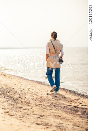 Back view of woman walking along the beach looking at the sun. Vertical shot. 120115292