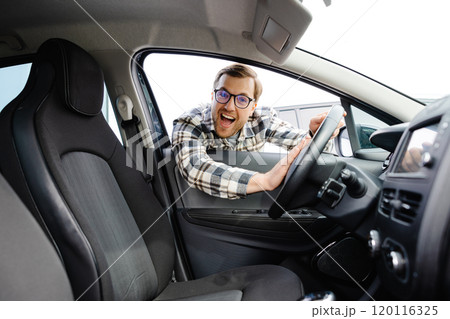 Young man looking through window inside new car, checking it before purchase at modern dealership store. Cheerful guy buying or renting automobile at showroom Young man looking through window inside new car, checking it before purchase at modern dealership store. Cheerful guy buying or renting automobile at showroom 120116325