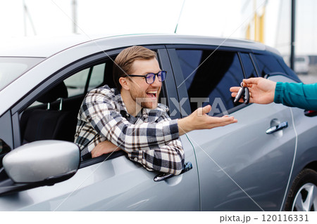 Salesman giving key to customer in modern auto dealership. Concept of choosing and buying new car at showroom 120116331