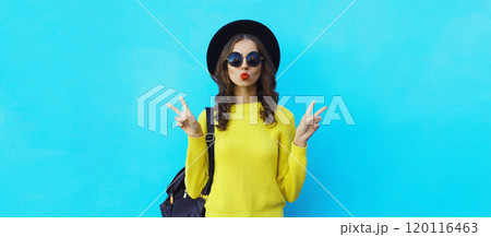 Portrait of stylish young woman in black hat, yellow sweater, modern cool girl posing on blue 120116463
