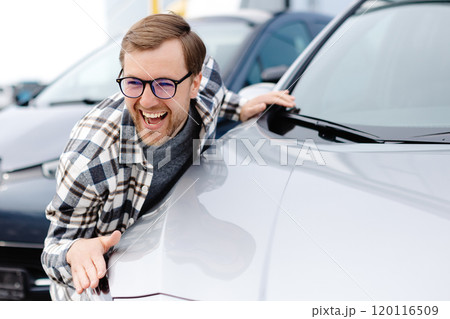 Young bearded man embracing his new car at the dealership smiling joyfully 120116509