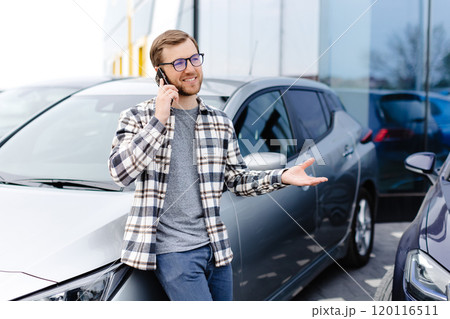 Handsome young man talking on the mobile phone and smiling while leaning at his car 120116511