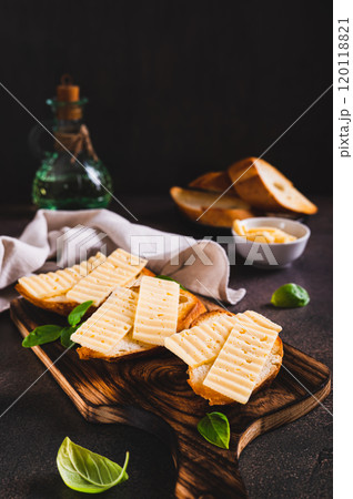 Delicious cheese sandwiches on toasts and basil leaves on a board on a table vertical view 120118821