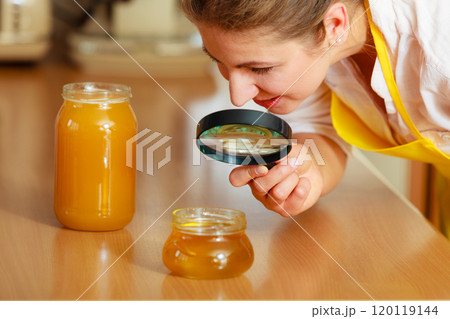 Woman inspecting honey with magnifying glass. Woman inspecting honey with magnifying glass. 120119144