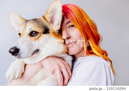 Young woman with vibrant orange and red hair embraces corgi dog against white background. Joyful bond between human and pet, feelings of happiness. Friendship and colorful lifestyle. 120119264