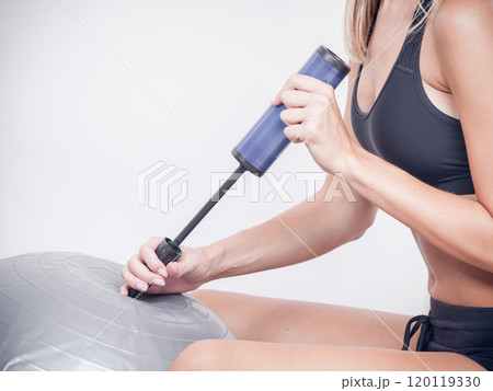 Fitness woman with air pump inflating fit ball 120119330