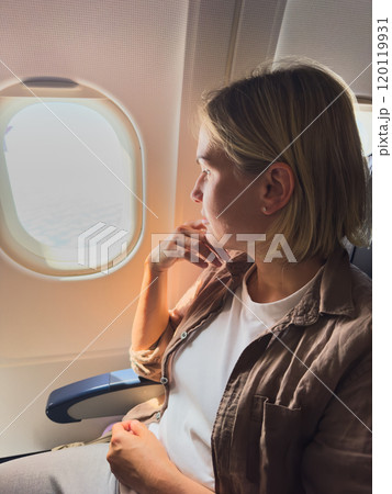 Passenger woman is flying in plane. Girl sitting in airplane looking out window going on trip vacation travel. Traveling female inside plane enjoying flight. Traveling girl Passenger woman is flying in plane. Girl sitting in airplane looking out window going on trip vacation travel. Traveling female inside plane enjoying flight. Traveling girl 120119931