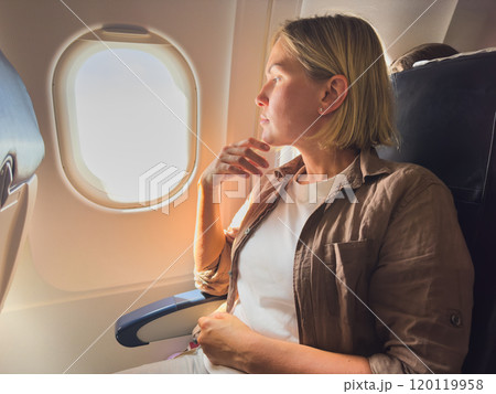 Passenger woman is flying in plane. Girl sitting in airplane looking out window going on trip vacation travel. Traveling female inside plane enjoying flight. Traveling girl Passenger woman is flying in plane. Girl sitting in airplane looking out window going on trip vacation travel. Traveling female inside plane enjoying flight. Traveling girl 120119958