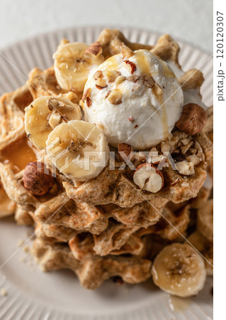 Homemade waffles stack with ice cream, bananas and nuts on white plate close up 120120307