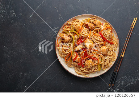 Asian udon noodles with chicken and vegetables sprinkled with sesame seeds on dark background top view Asian udon noodles with chicken and vegetables sprinkled with sesame seeds on dark background top view 120120357