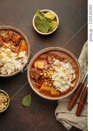 Two bowls of massaman curry with beef, potatoes, rice, and peanuts served in bowls top view, traditional Thai cuisine 120120362