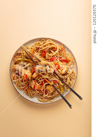 Asian chicken noodles with vegetables and chopsticks on beige background top view 120120370