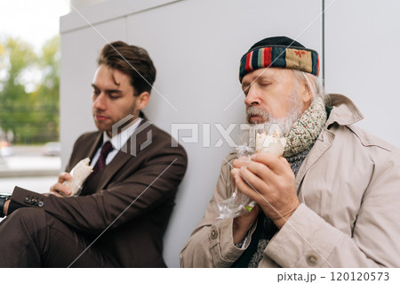 Kind young businessman in suit and elderly homeless man eating together sandwich on city street, bridging social divides with empathy and generosity, symbolizing charity and social inequality. 120120573