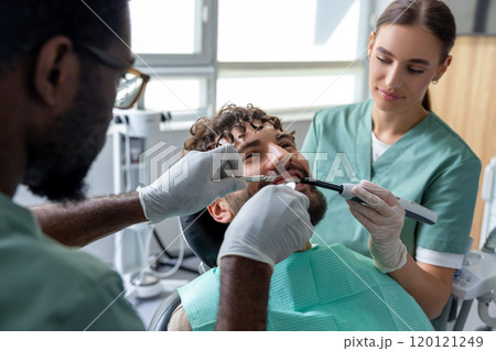Orthodontist conducting dental checkup in modern clinic examining patient's teeth 120121249