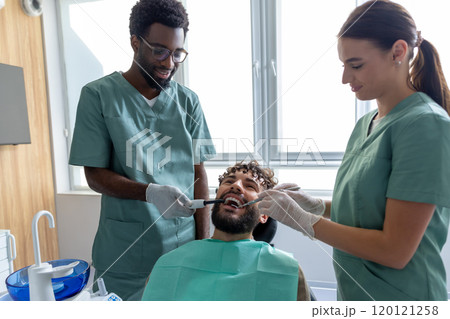 Male dentist examining patient’s teeth during checkup in dental office using orthodontic tools 120121258