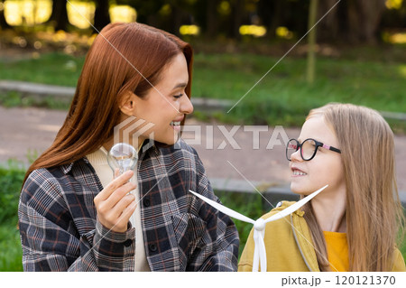 Little girl and teacher exploring wind turbine in park learning about eco-friendly energy Little girl and teacher exploring wind turbine in park learning about eco-friendly energy 120121370