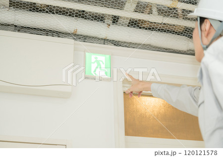 避難誘導灯を確認する消防設備士の作業着姿の女性 120121578