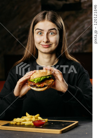 Playful woman enjoying a classic burger with fries and ketchup, perfect comfort food moment 120121846
