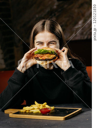 Excited woman holding a juicy burger with fresh toppings, capturing the joy of indulgent dining Excited woman holding a juicy burger with fresh toppings, capturing the joy of indulgent dining 120121850