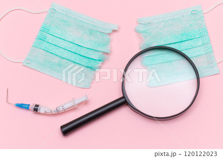 Broken Medical Syringe and Green Torn Medical Face Mask with Magnifying Glass 120122023