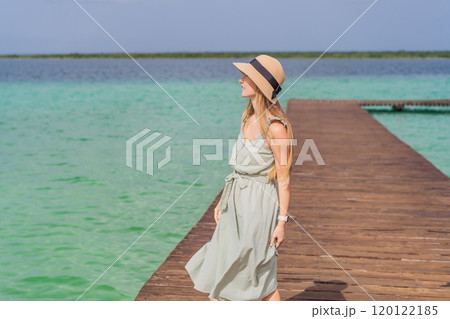 Female tourist in a turquoise dress standing on a wooden pier over the turquoise waters of Bacalar Lake, Mexico. Peaceful tropical travel destination concept 120122185