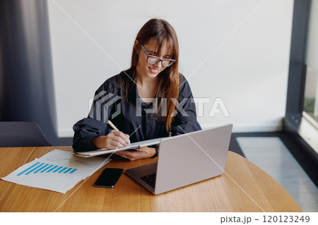 A Professional Woman Engaged in Remote Work Using Her Laptop Alongside Important Documents A Professional Woman Engaged in Remote Work Using Her Laptop Alongside Important Documents 120123249