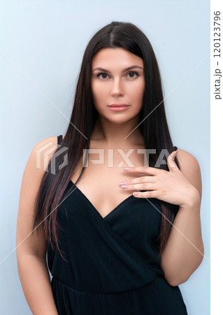 A portrait of a beautiful brunette in a black dress on a gray background. Studio photoshoot. 120123796