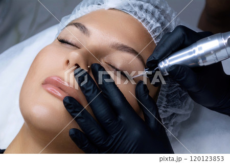 A beautician does permanent eyeliner makeup on a woman. Tattooing in a beauty salon. 120123853
