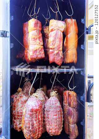 Smoker filled of with various cuts of meat, bacon hanging from hooks racks combine to create culinary tradition delicious treat in smokehouse 120127552