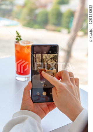 A woman is filming a grapefruit ade on a table with her cell phone 120128632