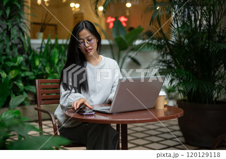 An attractive Asian woman is about to check messages on her phone while working remotely from a cafe 120129118