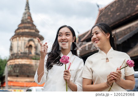 Two beautiful, smiling Asian women stand in a temple, enjoying a conversation together. Two beautiful, smiling Asian women stand in a temple, enjoying a conversation together. 120129368