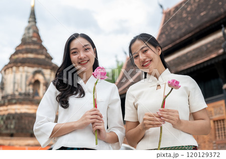 Two beautiful Asian women are holding pink lotuses and smiling at the camera. Two beautiful Asian women are holding pink lotuses and smiling at the camera. 120129372