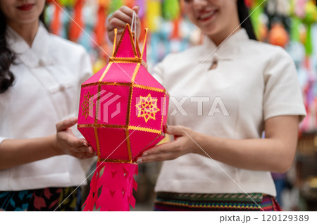 A close-up of two charming Asian women in traditional dresses hold a lantern together. A close-up of two charming Asian women in traditional dresses hold a lantern together. 120129389